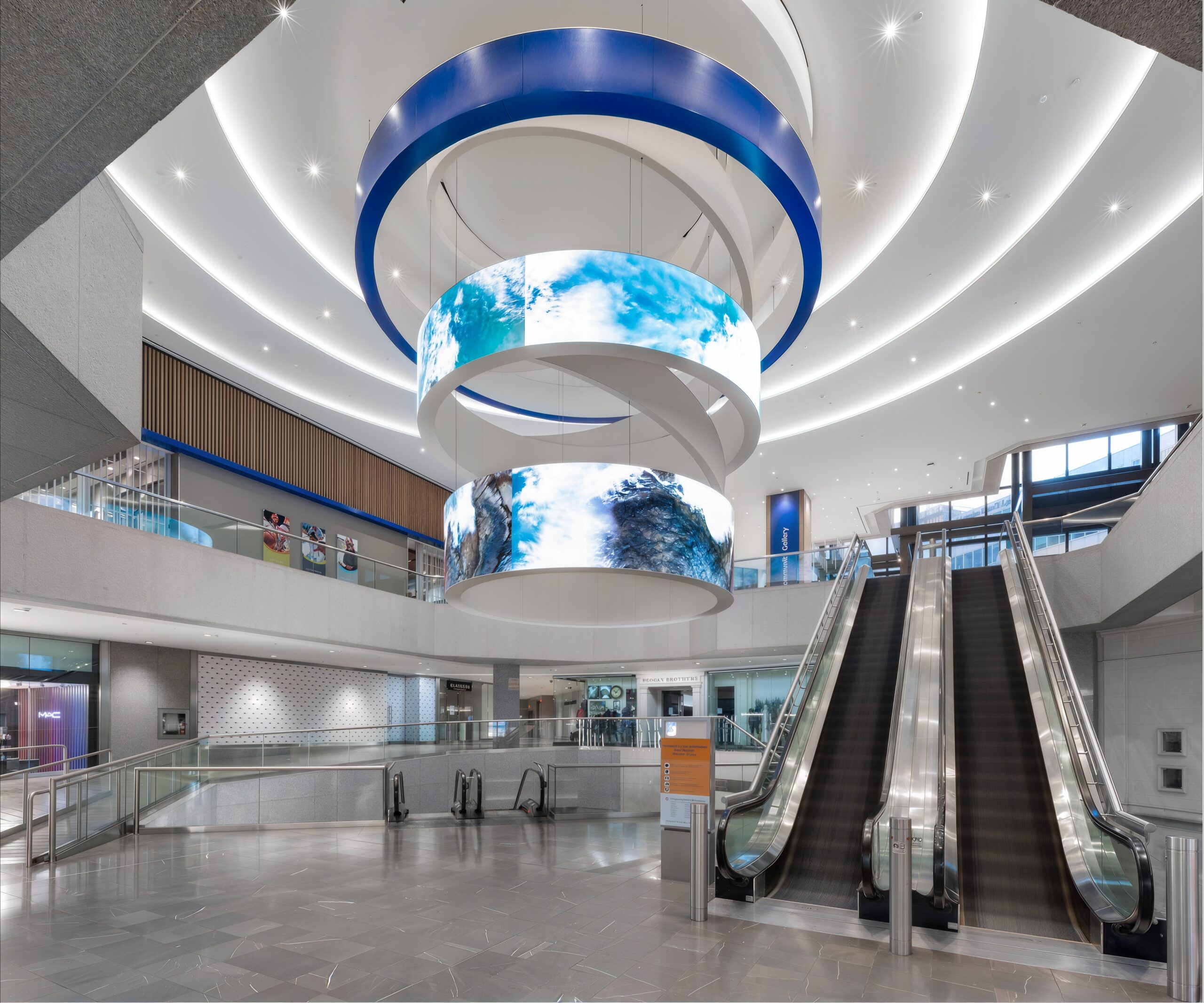 A modern interior space with illuminated circular LED displays, escalators, and contemporary architecture.